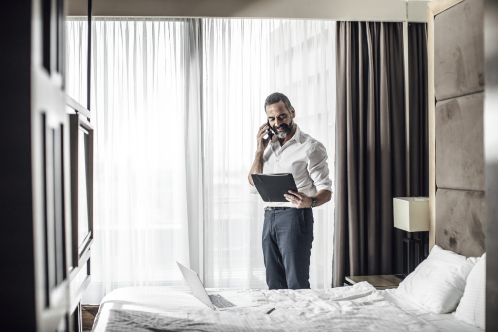 Middle-aged businessman standing at bedroom and talking on mobile phone.