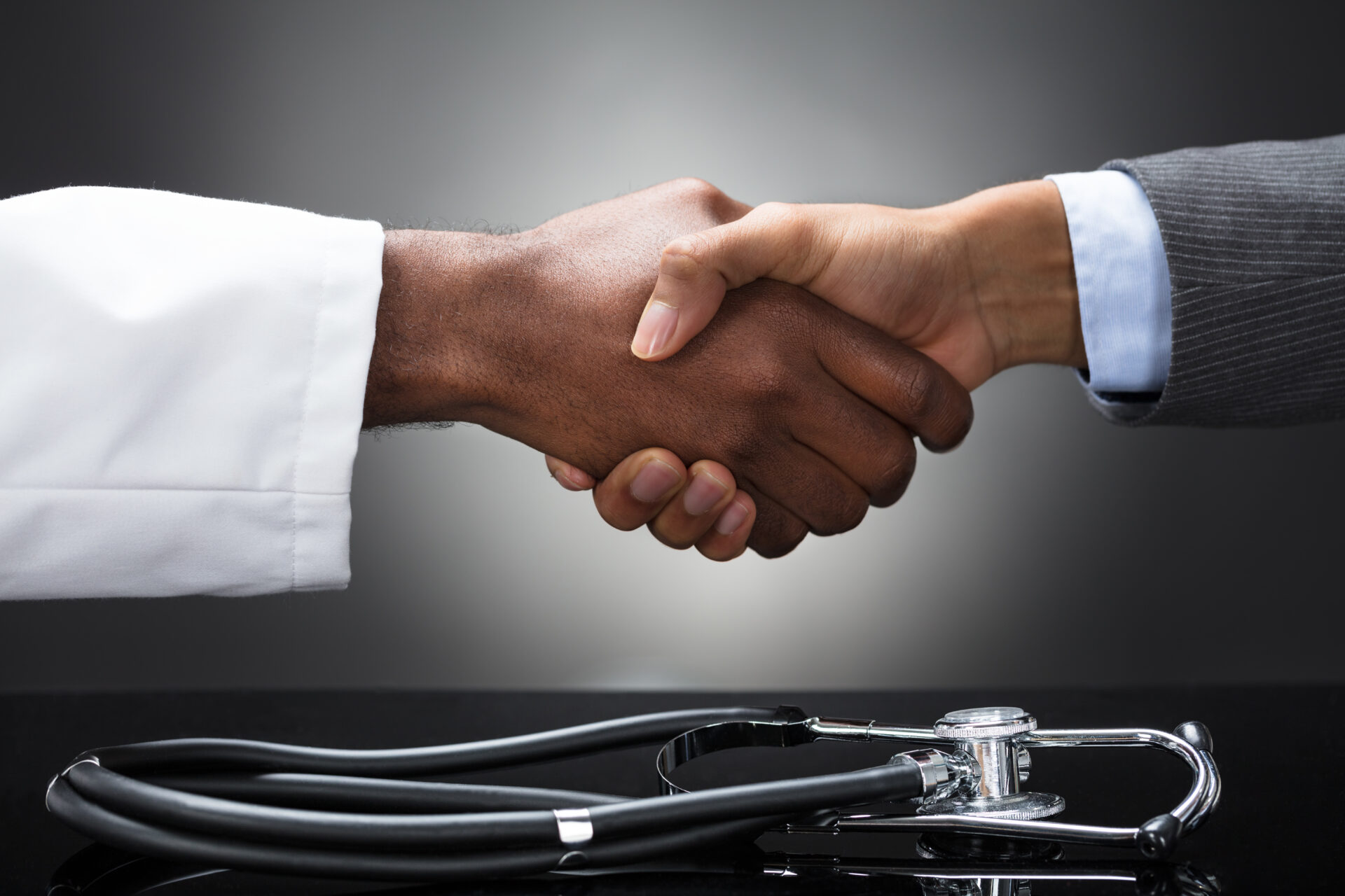 Doctor and business man shaking hands over a stethoscope